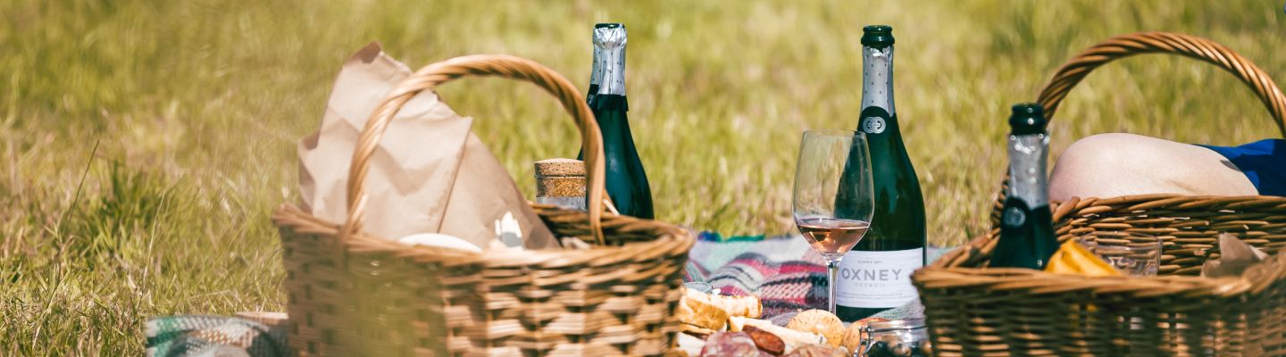Picnic hampers and bottles of wine laid out on a picnic blanket at Oxney Organic Estate